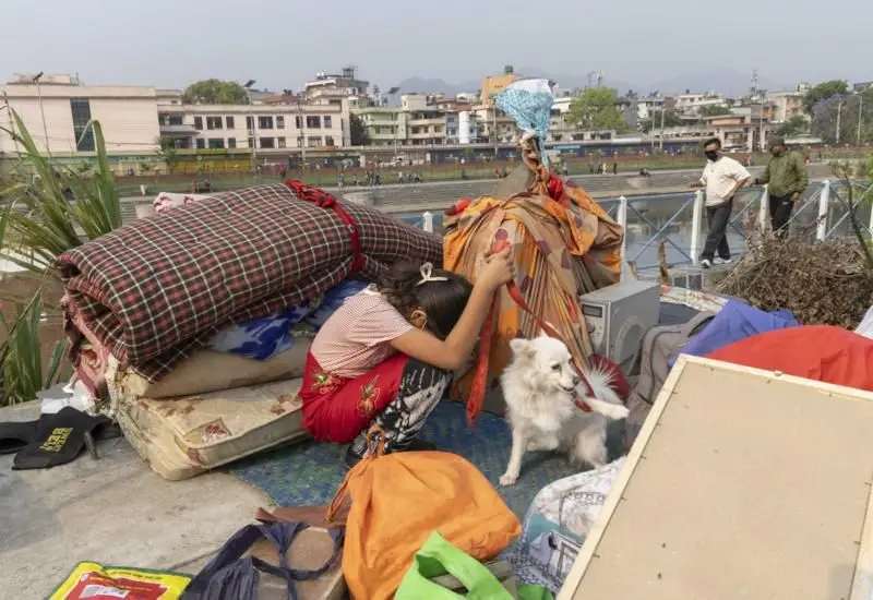 सुकुम्बासी बस्तीमा घरायसी समानहरू बीच कुकुर समातेर बसेकी एक बालिका