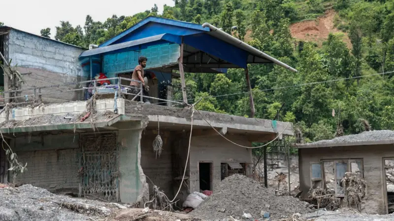 धादिङमा त्रिशूली नदीनजिकै बाढी पसेको तर नभत्किएको एउटा घरमा सरसफाइ गर्दै एक व्यक्ति