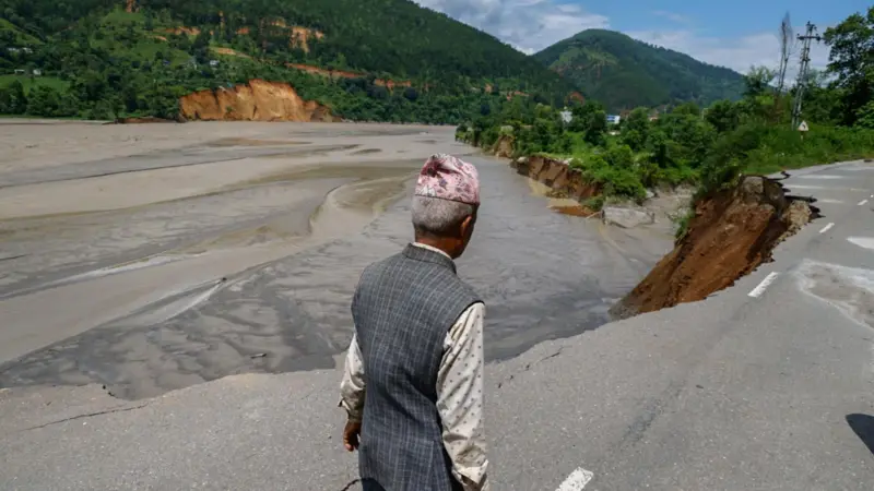 धादिङमा त्रिशूली नदीले कटान गरेको सडकमा हिँड्दै एक व्यक्ति